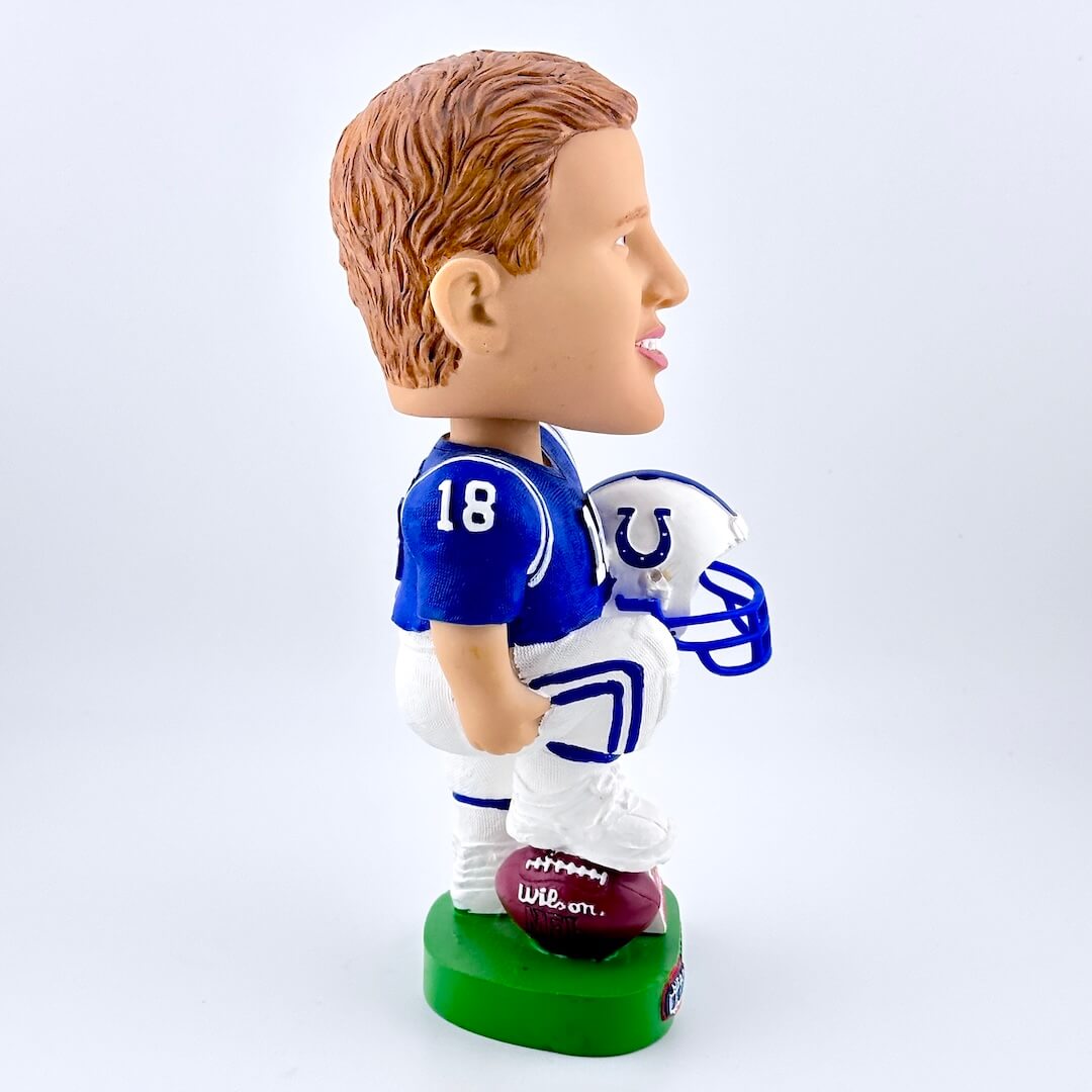 Football player bobblehead in blue jersey holding white helmet against white background. 