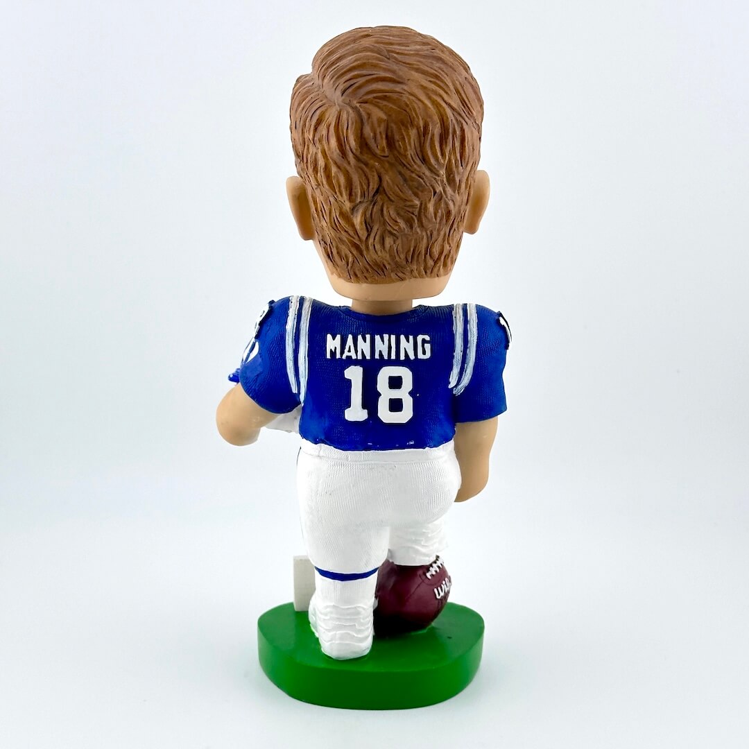 Football player bobblehead in blue jersey holding white helmet against white background. 