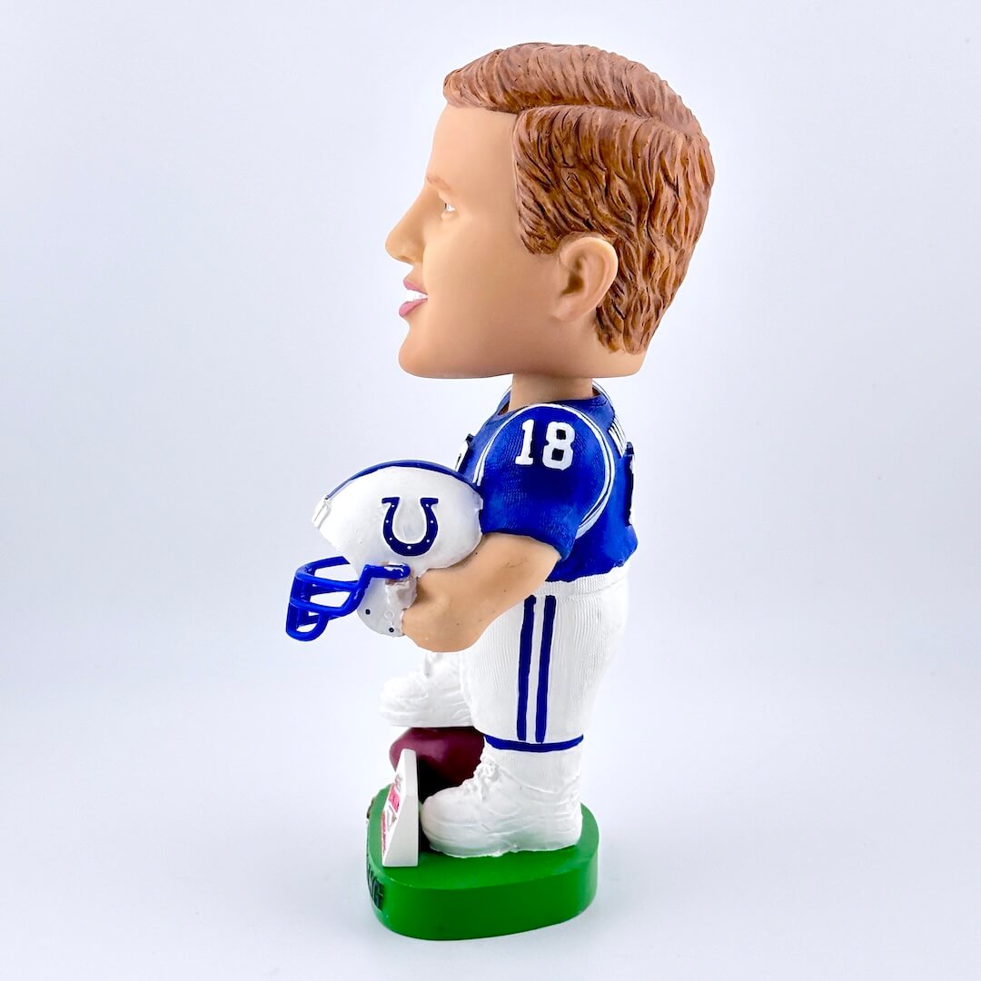 Football player bobblehead in blue jersey holding white helmet against white background. 