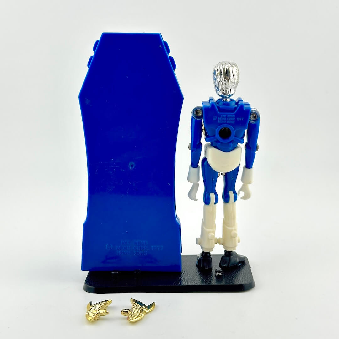 A blue and white action figure standing next to a blue sarcophagus accessory, with two small gold accessories placed in front.