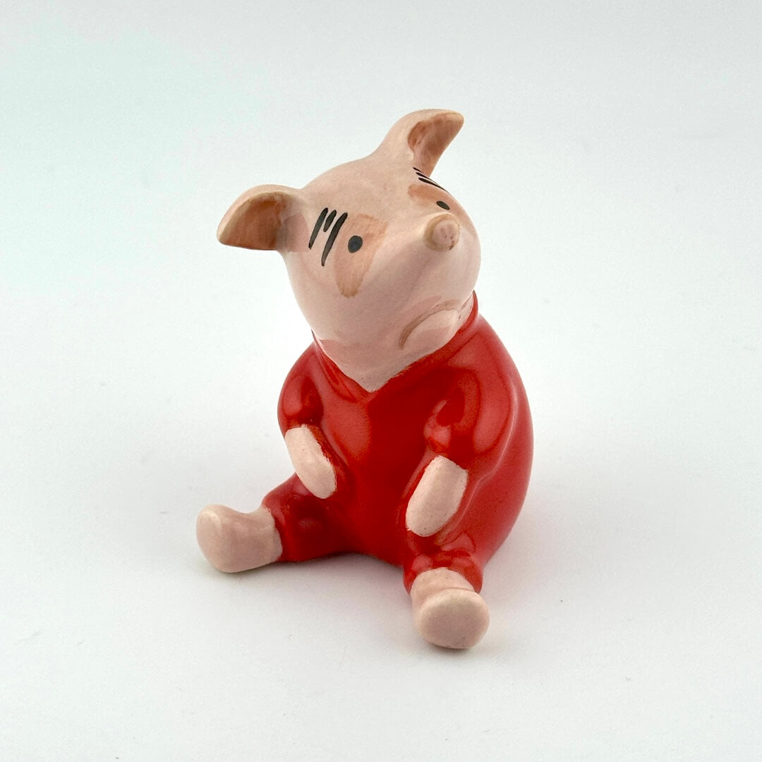 A small glossy ceramic pig figurine wearing a red outfit, seated against a plain white background.