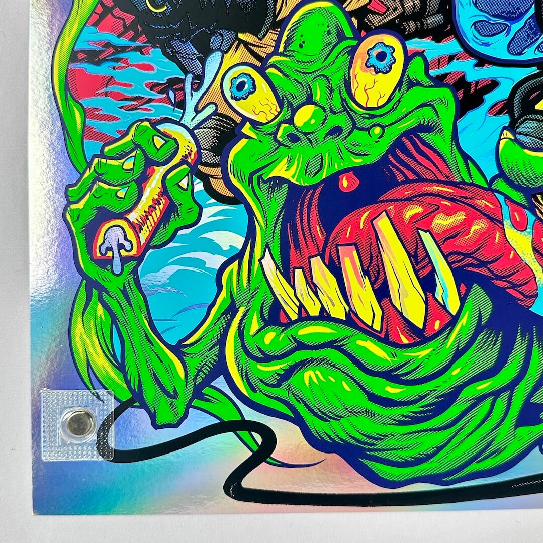 Bottom left corner of poster with colorful illustration of a creature with sharp teeth on a rainbow foil poster.
