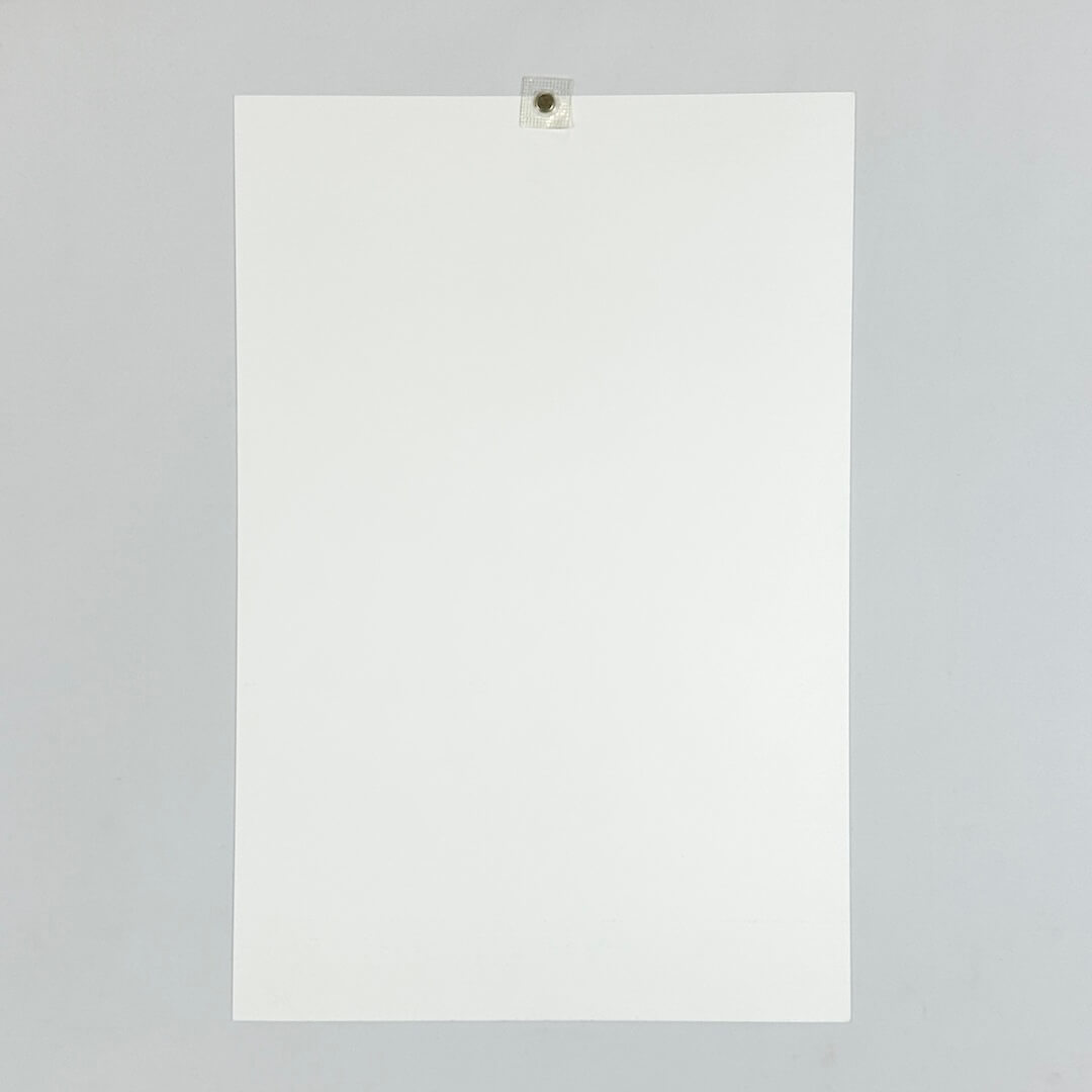 Reverse side of print. A plain white sheet displayed on a plain white background, held up by a magnet. 