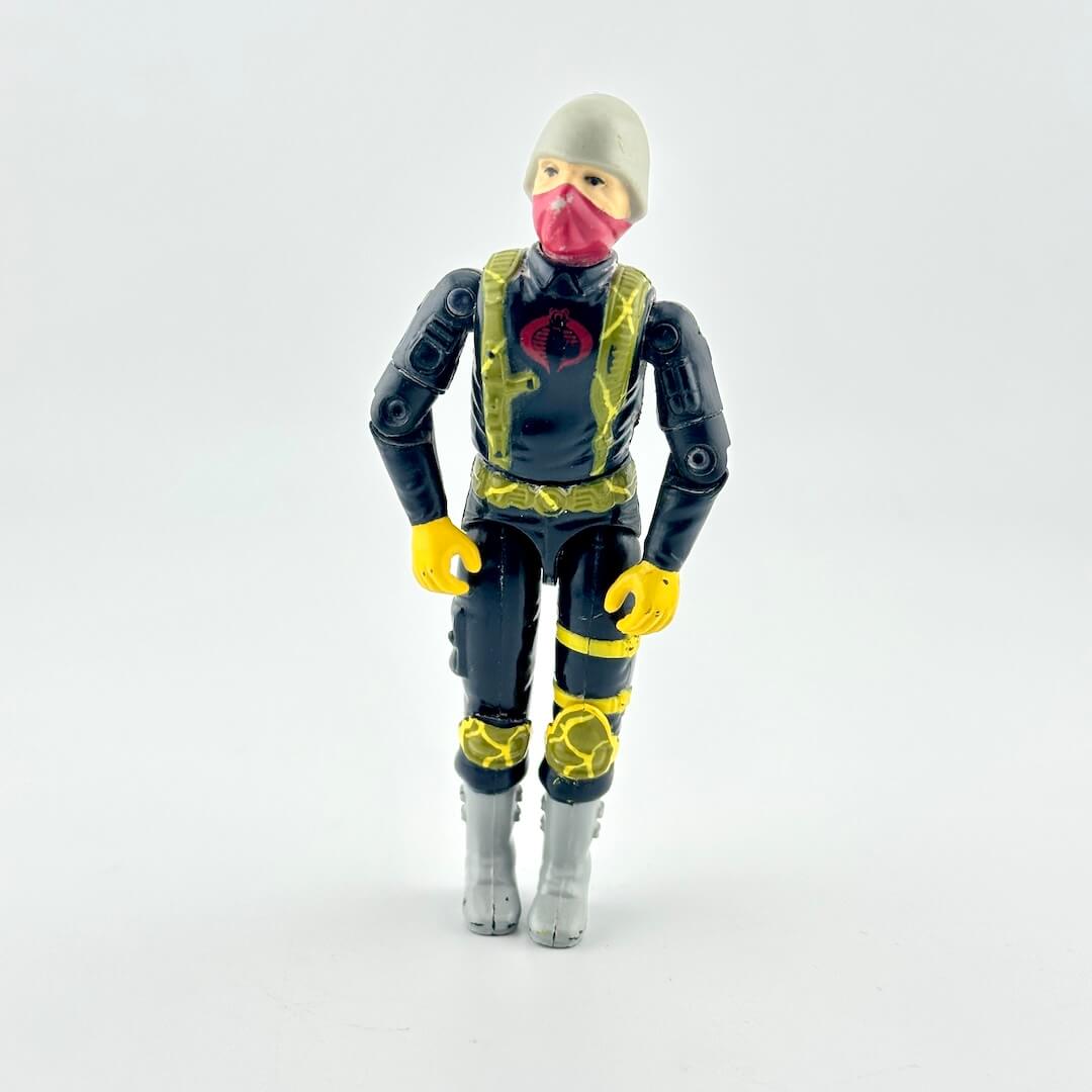 A toy action figure of a character wearing a gray beanie, pink face mask, black and yellow suit, and gray boots.