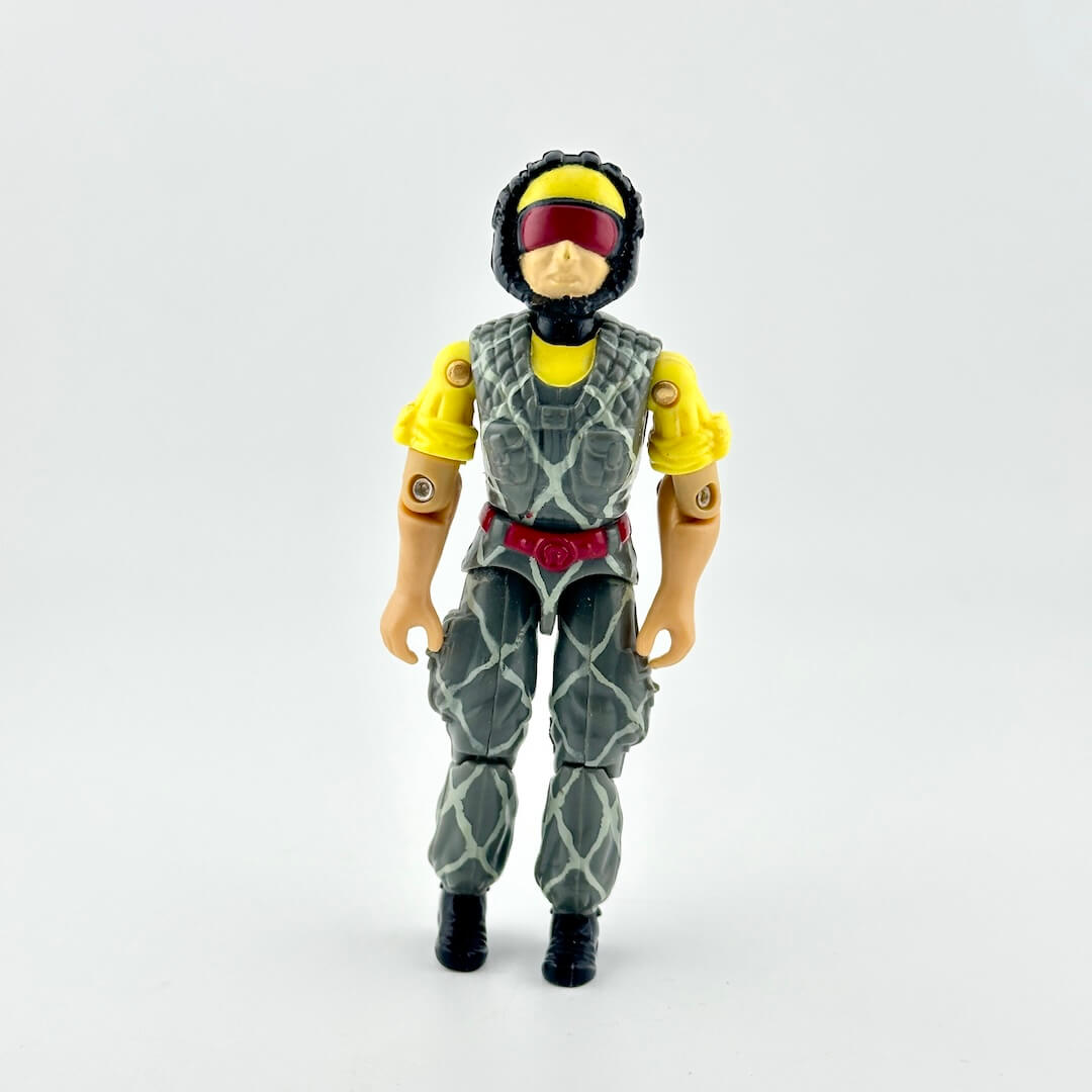 Action figure wearing a gray and green camouflage patterned suit with yellow sleeves, a red visor, and a yellow helmet.