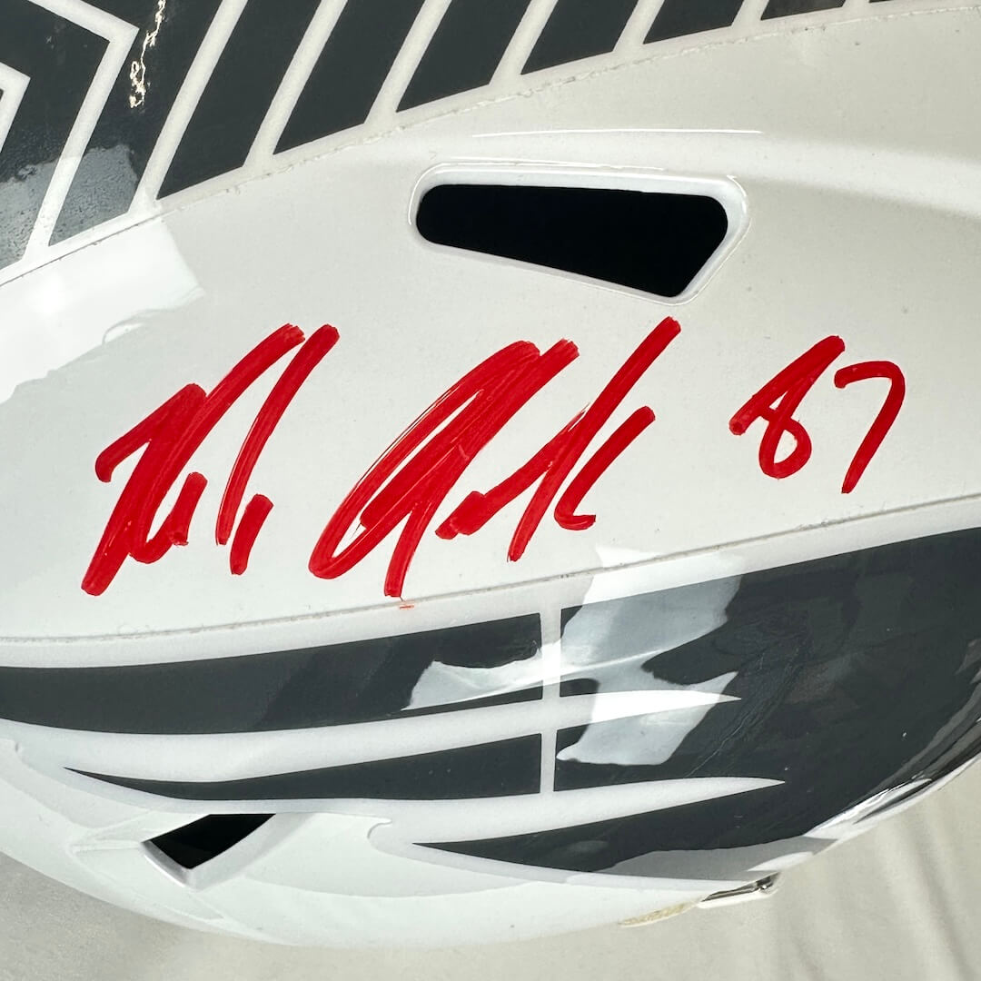 Close-up of a white helmet with red signature and number 87 on a black background