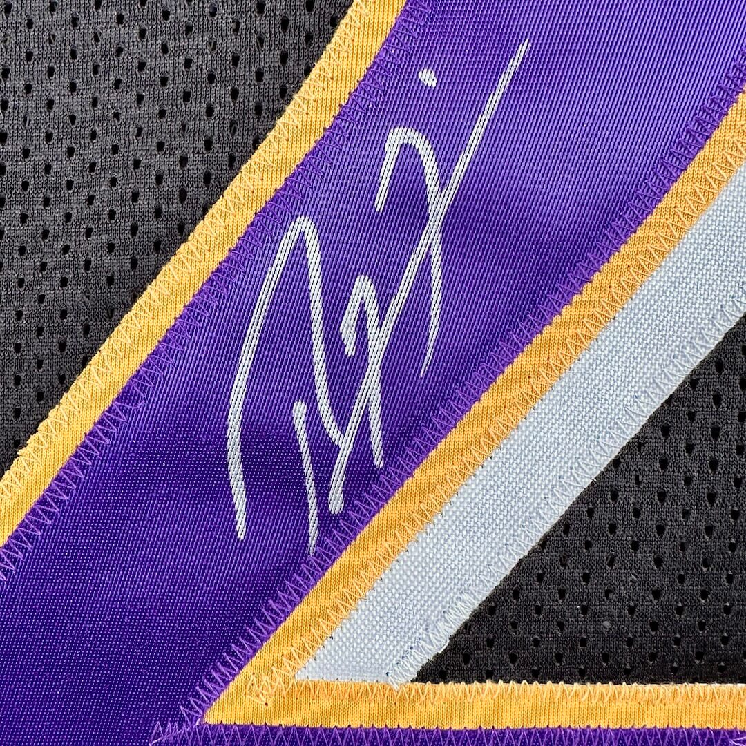 Close-up of a sports jersey with a signature on a purple, yellow, and gray background