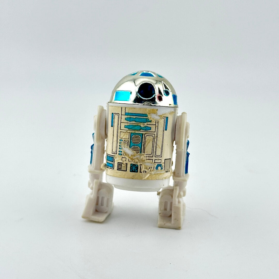 A small R2-D2 droid figurine with a metallic silver dome, white body, and blue and gold panel details.
