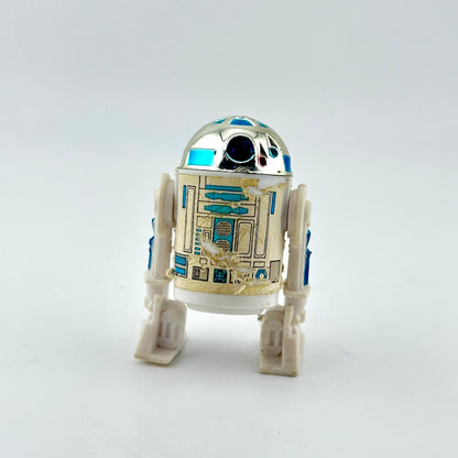 A small R2-D2 droid figurine with a metallic silver dome, white body, and blue and gold panel details.