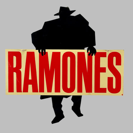 Black silhouette of man in hat behind tan banner with large red "RAMONES" printed in clear text.