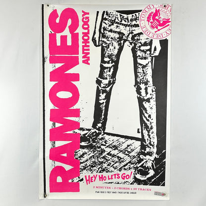 Poster of Ramones Anthology with pink text and black and white graphic of legs wearing jeans.