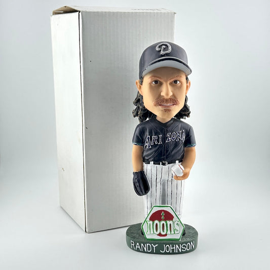 Bobblehead figure of a baseball player with a cap and jersey, standing next to a box on a light gray background.
