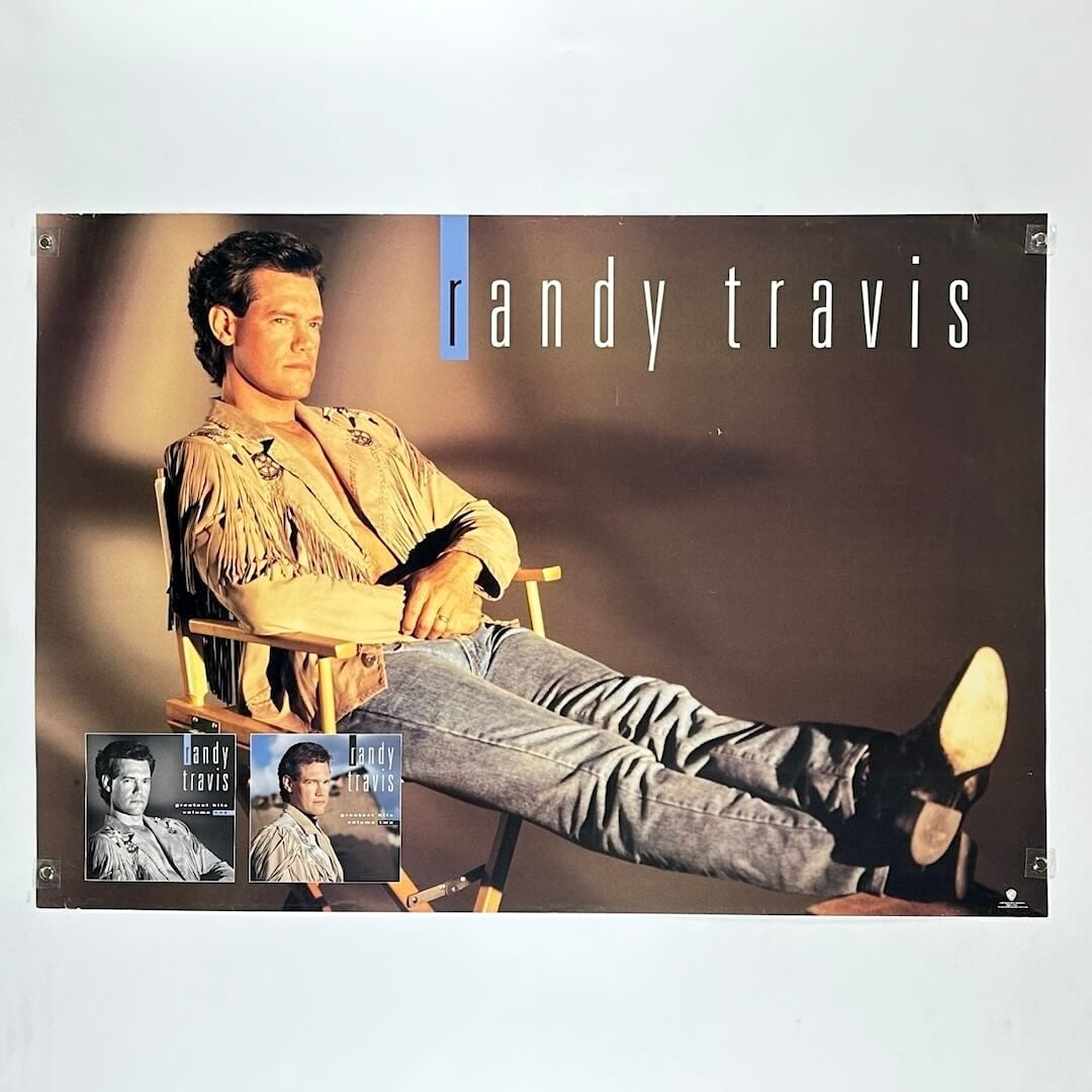 Randy Travis poster with a man sitting in a chair, wearing a beige jacket and gray pants.