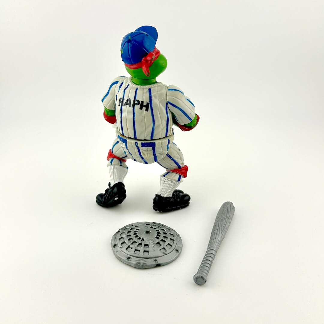 Toy figure of a character with a blue hat and striped uniform, standing next to a manhole cover and bat on a white background.