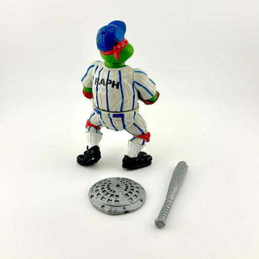 Toy figure of a character with a blue hat and striped uniform, standing next to a manhole cover and bat on a white background.