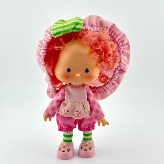 Toy doll with pink outfit and large flower hat on a white background