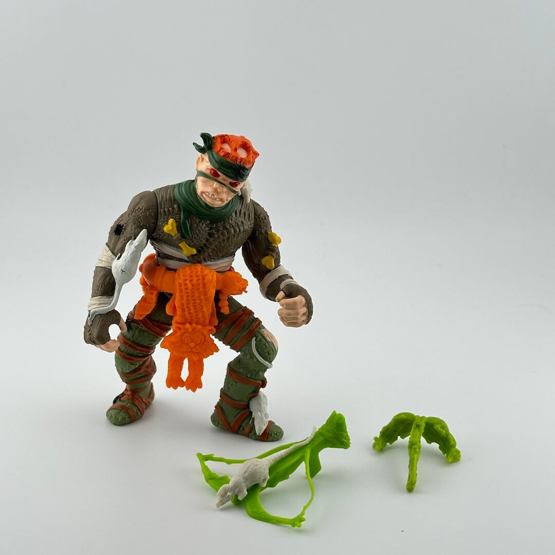 White male figure  with red eyes, dressed like mummy with orange belt and lime green accessories, 3 white rats riding on figure. 