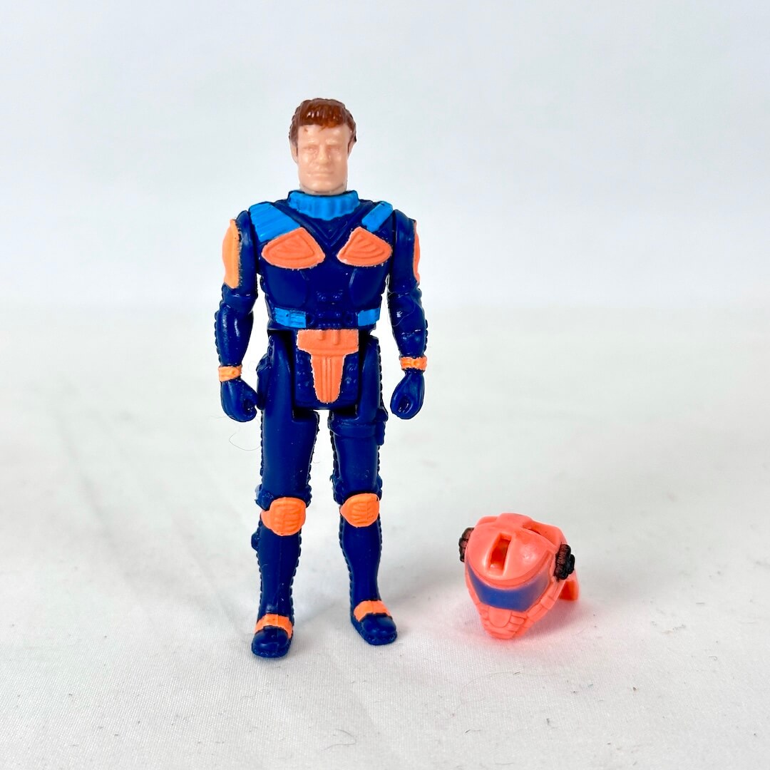A vintage blue and orange action figure standing next to its detached orange helmet on a plain white background.