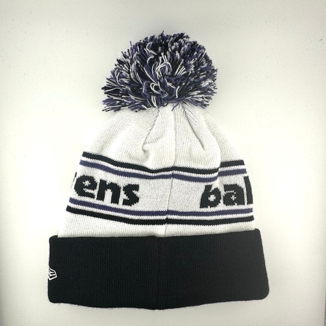 White knit cap with black/purple stripes around black text, black cuff with Ravens logo front center & black/white/purple pom