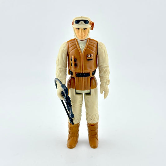 Action figure in beige outfit with brown vest and boots holding weapon on white background. 