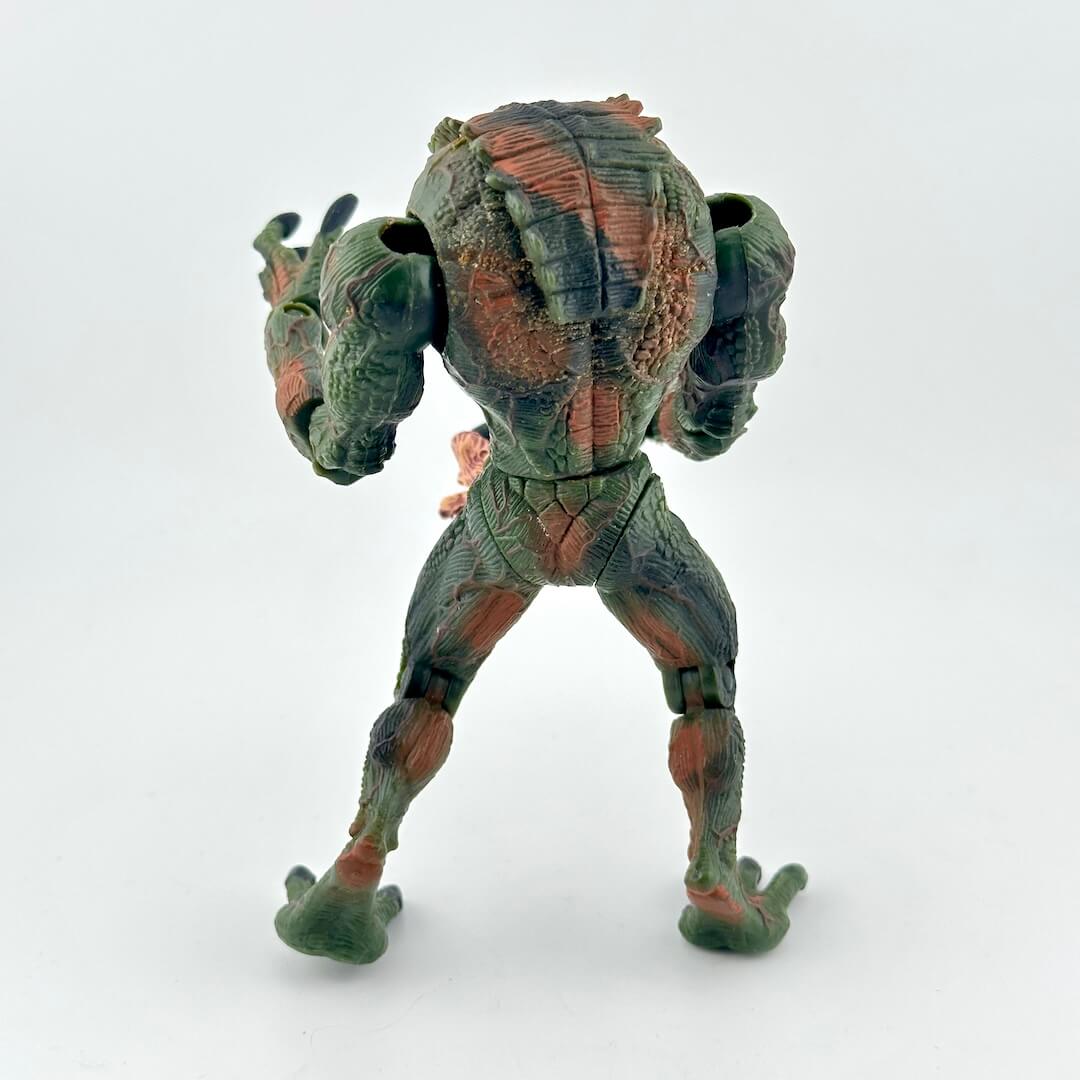 A back view of a green and brown textured action figure on a plain white background.