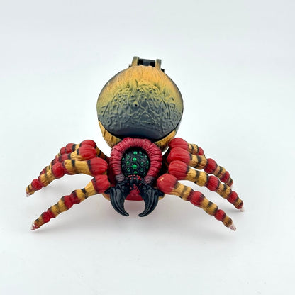 A spider action figure with a textured gold and black abdomen, red and yellow banded legs, and a central green eye.