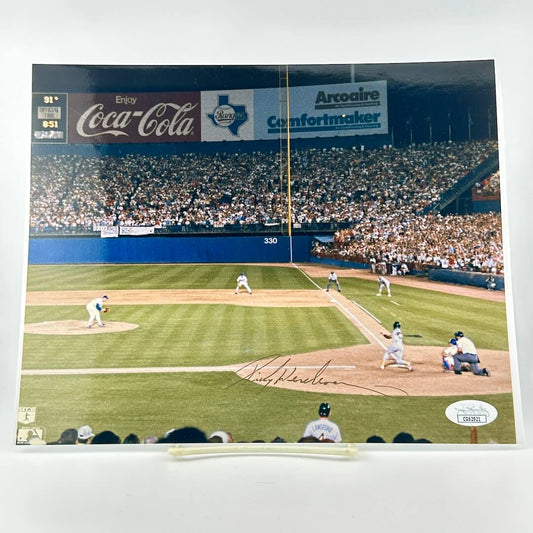 Color photograph of baseball field with players and gold signature against white background. 