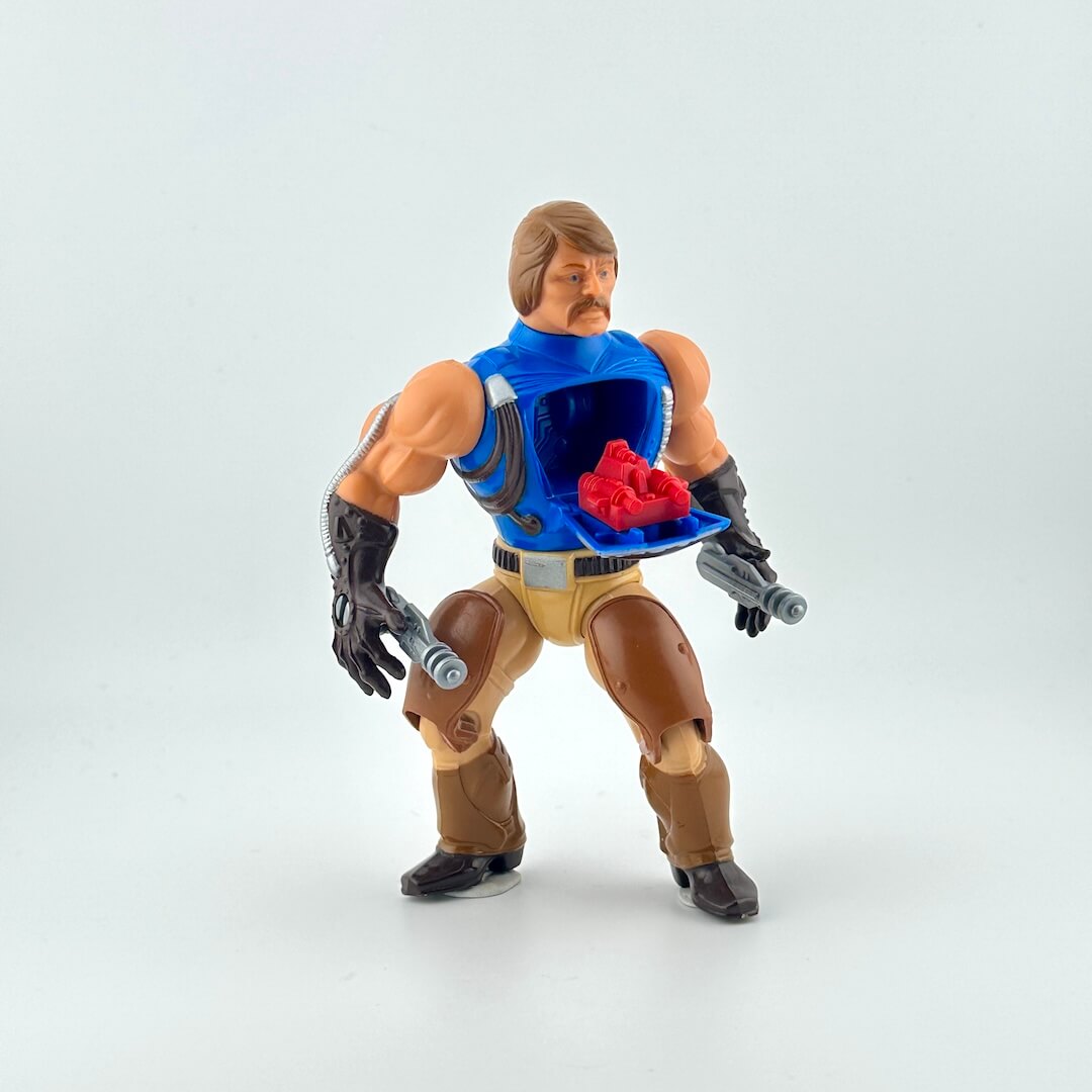 Action figure with blue vest and brown pants on a white background with open chest showing red gun.