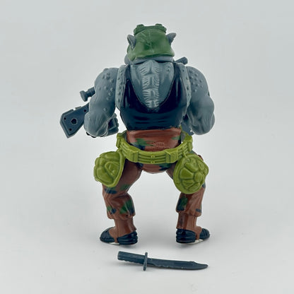 Anthropomorphized Rhino with in brown outfit, green belt with turtle shells, grey trash can lid shield, grey gun, and grey knife. Back.