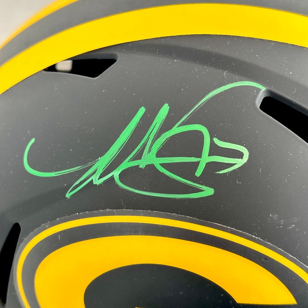 Close-up of a black and yellow football helmet featuring a green autograph on the side.