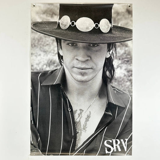 Black and white portrait of a person wearing a wide-brimmed hat with decorative elements, set against a natural background.