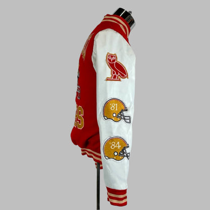 Side view Backside of varsity jacket with red body, white sleeves with two helmet patches down sleeve under owl logo. 