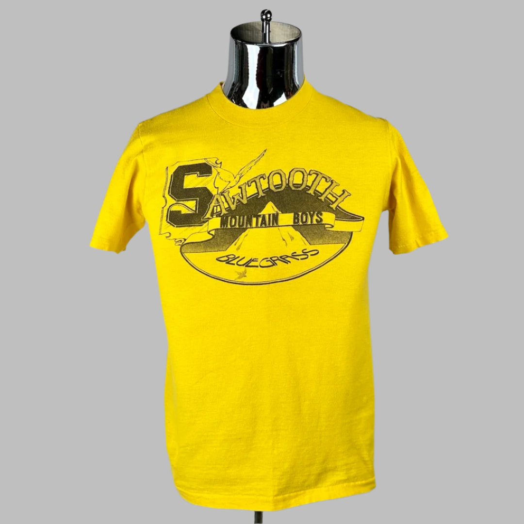 Yellow short sleeve t-shirt with Sawtooth Mountain Boys Bluegrass printed in black in front of mountain silhouette in backgroun. 