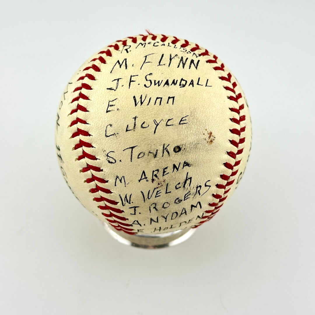 A vintage autographed baseball on a clear display stand, featuring black ink signatures around the red stitching.