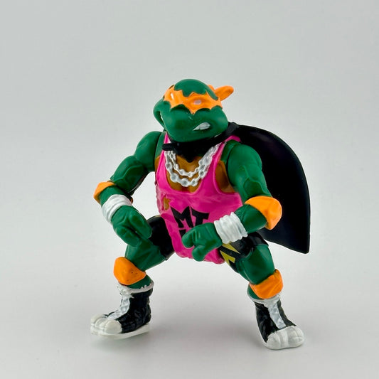 Anthropomorphized turtle wearing pink jersey, orange protective gear, black cape, & white jewelry. Front.