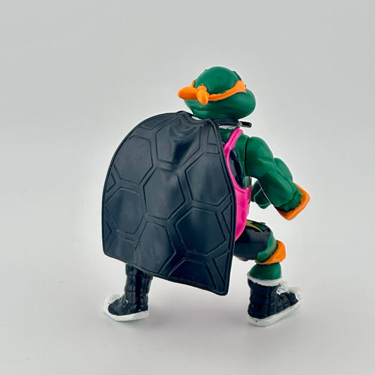 Anthropomorphized turtle wearing pink jersey, orange protective gear, black cape, & white jewelry. Back.