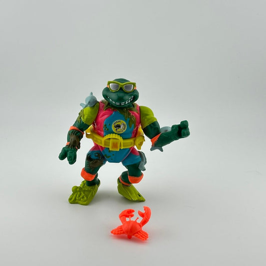 Anthropomorphized turtle wearing yellow belt, green shoes, pink & blue wetsuit; front view. With orange crab.