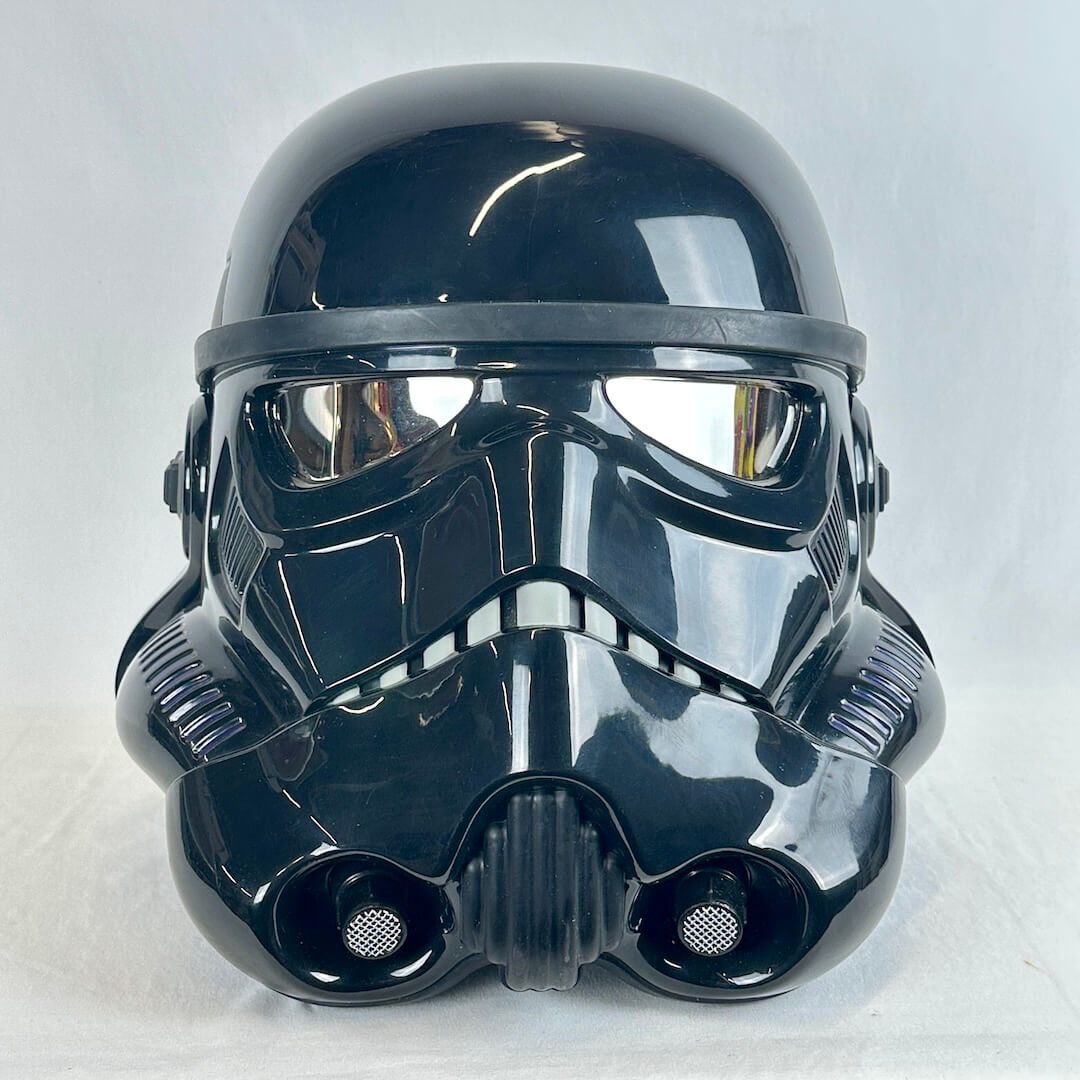A glossy black Stormtrooper-style helmet photographed against a plain light gray fabric background.