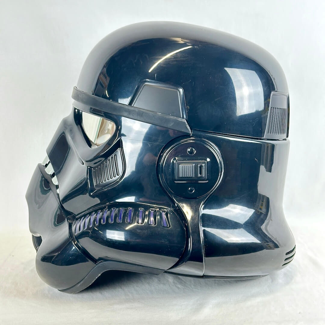 A glossy black stormtrooper helmet, photographed from a side profile against a white fabric background.