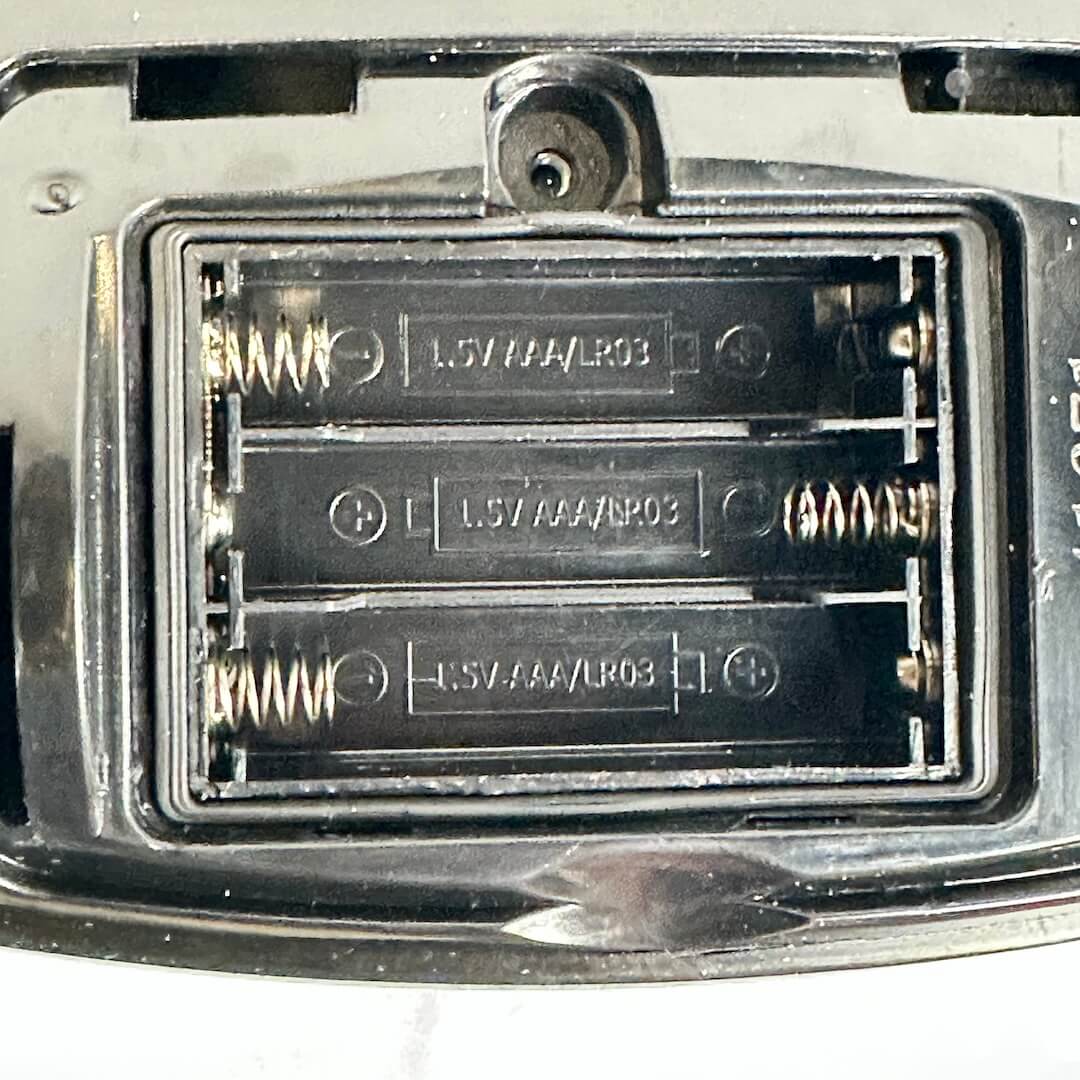Up close photo of lack battery compartment for three AAA batteries, with springs. 