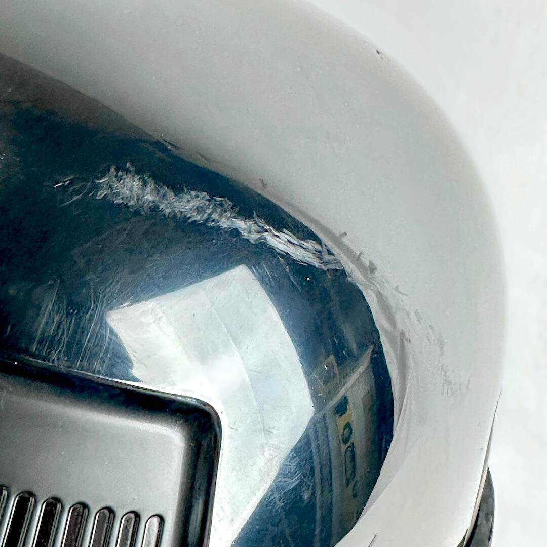 Close-up of a dark reflective surface showing scratches and scuffs alongside a black vented panel.