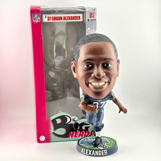 Football player bobblehead holding a football in front of NFL branded packaging against white background. 