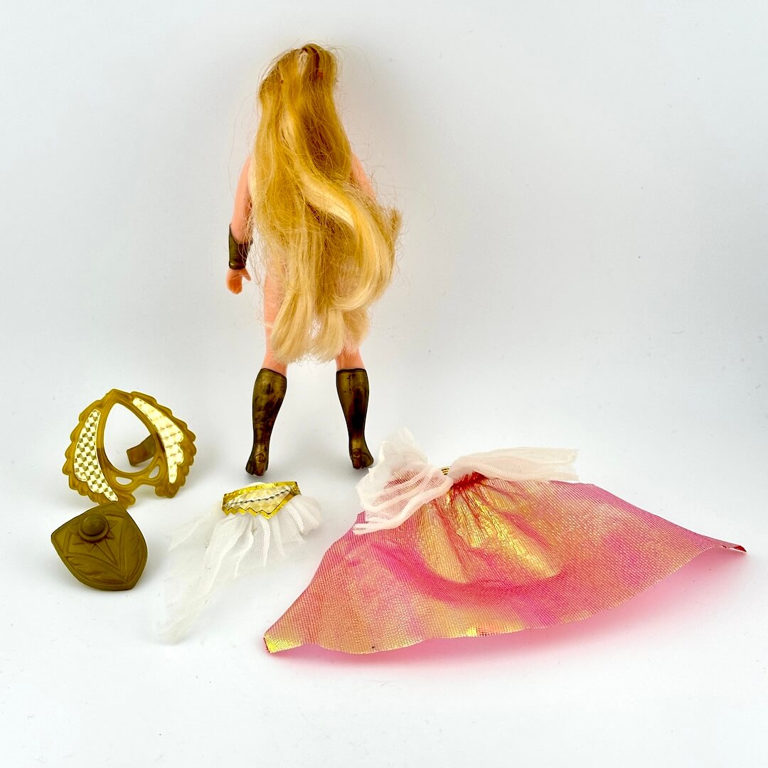 Blonde She-Ra doll with accessories on white background.