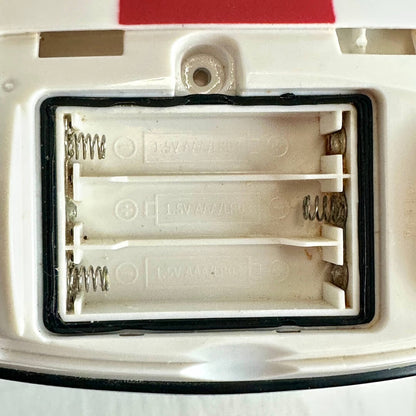 Close-up of a white plastic battery compartment with three slots, metal spring terminals, and a black rubber gasket.