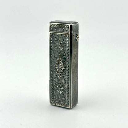A vintage silver pocket lighter with ornate engraved floral and geometric patterns on its rectangular body.