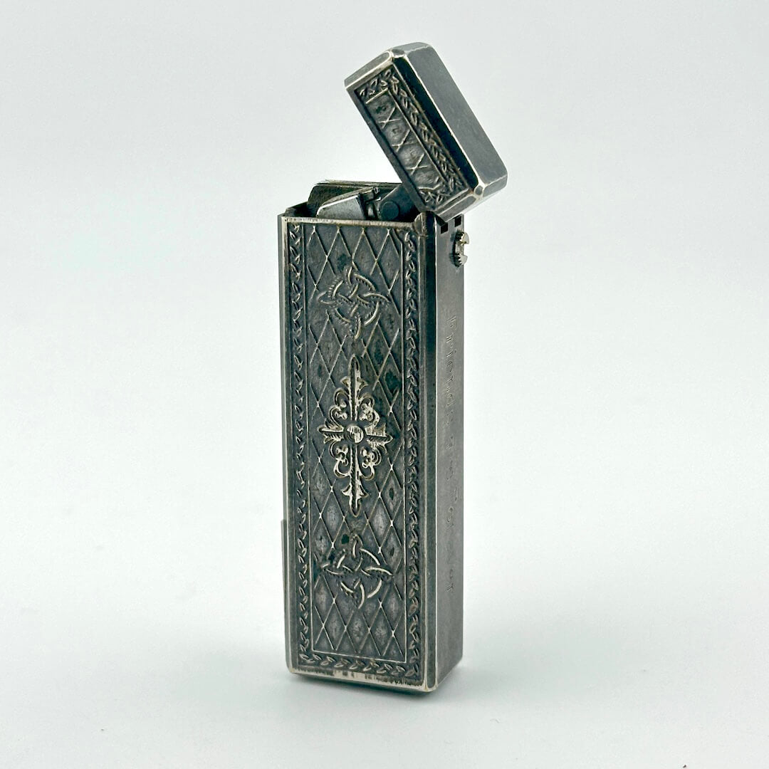 A vintage silver pocket lighter with ornate embossed floral and diamond patterns.