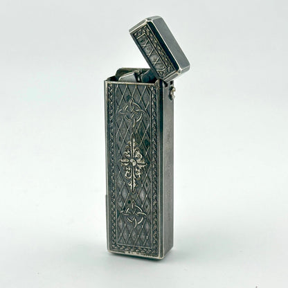 A vintage silver pocket lighter with ornate embossed floral and diamond patterns.