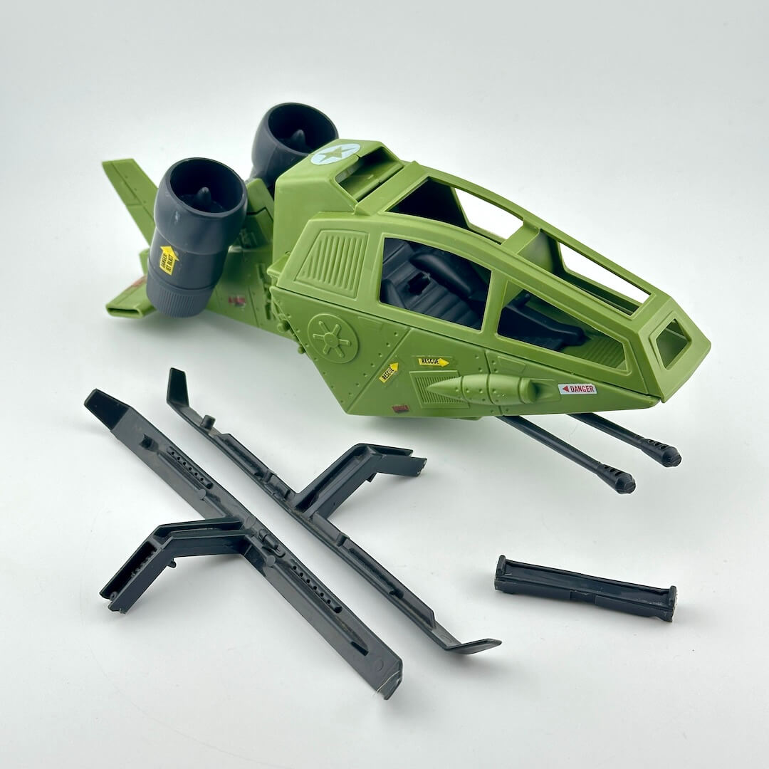 An olive green toy fighter jet model with black engines and accessories, displayed on a clean white background.
