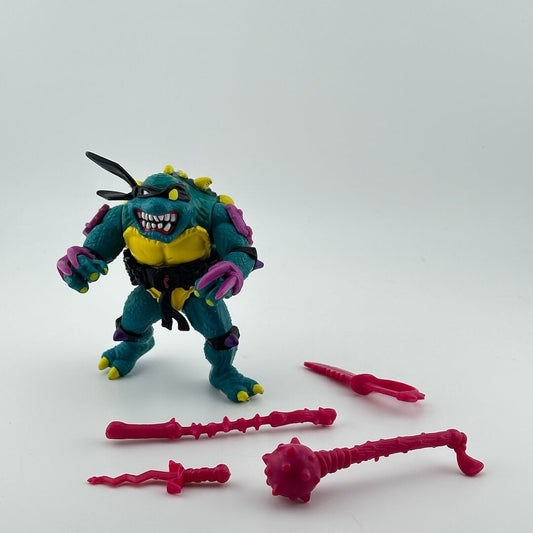 Anthropomorphized turtle bearing its teeth in black mask with purple armor pieces, pictured with pink accessories.
