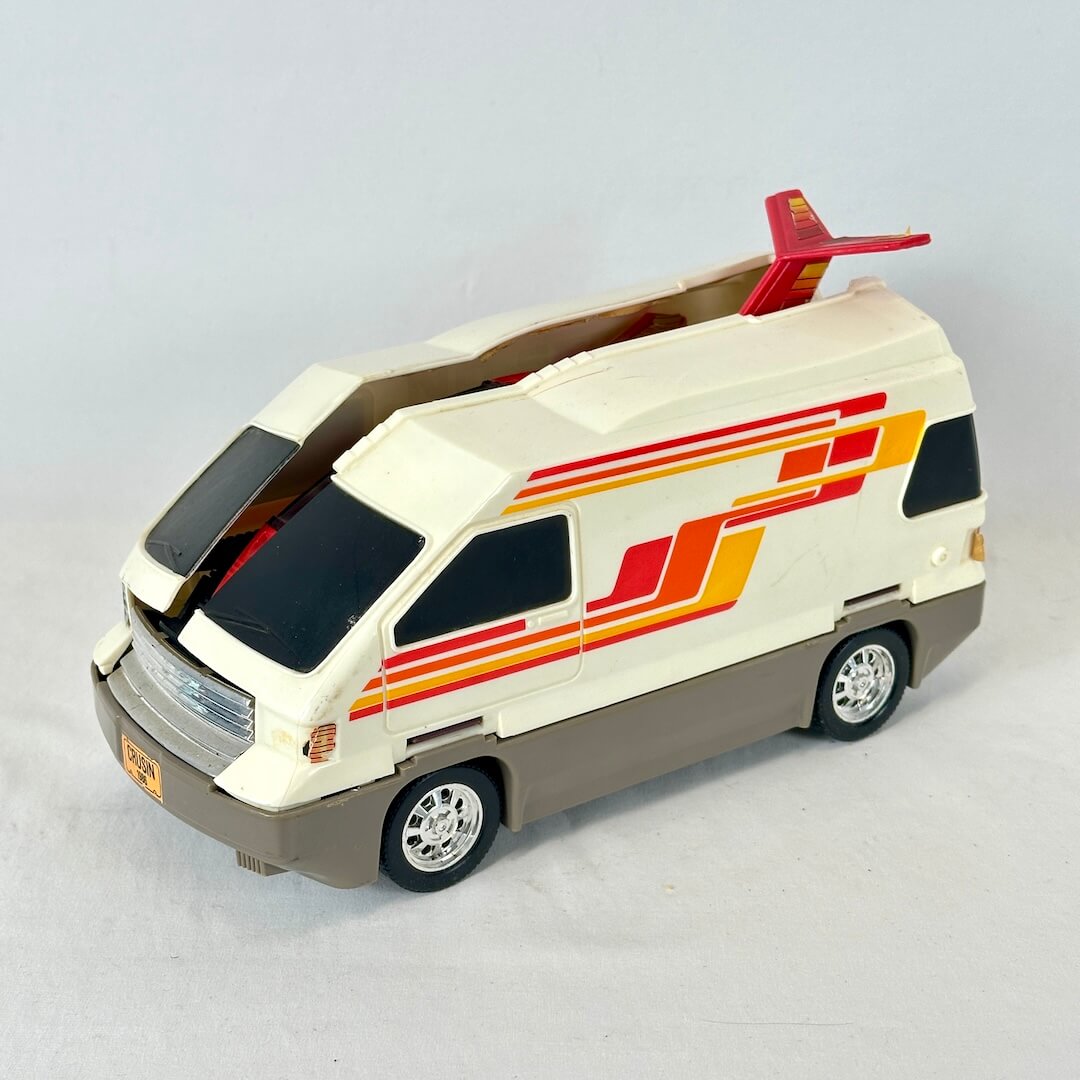 A vintage toy van with a red jet attached to the roof, photographed on a light gray studio background.